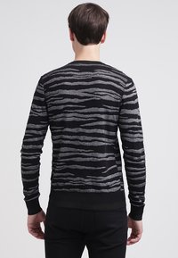 Czarny sweter z srebrnym falistym wzorem, wykonany z miękkiego materiału dzianinowego, z okrągłym dekoltem i ściągaczami na rękawach, noszony z czarnymi spodniami.