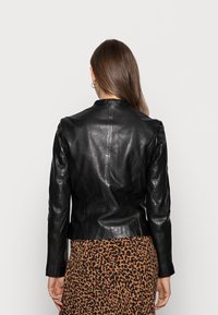 Svart läderjacka med en figurnära design och rund hals. Slät textur, långa ärmar och sömmar synliga på ryggen. Matchad med en kjol i leopardmönster.