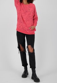 Felpa rosa con motivo floreale, con polsini e orlo a costine. Abbinata a jeans neri strappati e stivali neri grossi.