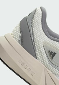 Kevyt urheilukengät, joissa on teksturoitu vaaleanbeige päällinen, harmaita yksityiskohtia ja huomiota herättävä "LIGHTSTRIKE"-logo vaalean kremi-kumipohjassa.