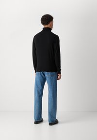 Μαύρο πλέκτο πουλόβερ με ψηλό γιακά, σε συνδυασμό με ανοιχτό γαλάζιο τζιν με ίσια γραμμή. Το ύφασμα φαίνεται λείο και ελαφρώς υφασμένο.