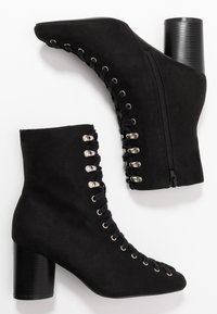 Botas de tobillo de ante negro con punta afilada, diseño de cordones, ojales plateados, cremallera lateral y tacón grueso negro.