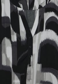 Blouse à motifs noir et blanc avec un col en V et des boutons, en tissu doux avec un design de coups de pinceau et des manches courtes.