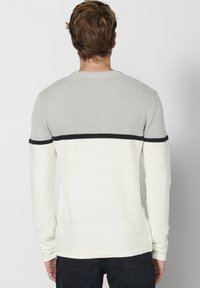 Maglione a maniche lunghe con parte superiore grigia chiara a trama e sezione inferiore bianca a righe, con una striscia di accentuazione blu navy lungo la cucitura.