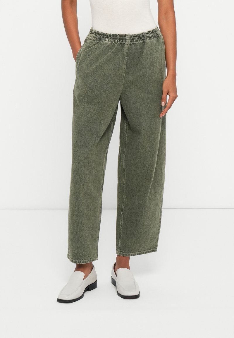 Zaļas džinsu bikses ar elastīgu jostu, sānu kabatām un brīvāka piegriezuma. Audums izskatās mīksts ar nedaudz teksturētu apdari.