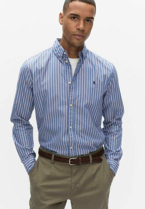 Blå og hvide stribet skjorte med knapper, røde detaljer, lange ærmer, krave, kombineret med brunt flettet bælte og beige bukser.