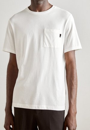 T-shirt blanc à manches courtes en coton avec une poche poitrine et un petit détail d'étiquette noire, doté d'un col rond et d'une coupe décontractée.