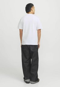 Hvid bomulds t-shirt, korte ærmer, parret med mørke denim wide-leg bukser, foldede manchetter, kontrast syning og et bælte.