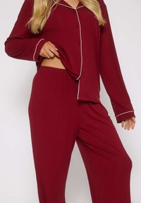 Set di pigiama a coste color borgogna con piping bianco. Caratterizzato da maniche lunghe, bottoni sulla maglia e cintura elastica nei pantaloni.