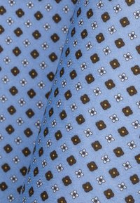 Jasnoniebieska tkanina z powtarzającym się wzorem brązowych diamentów i małych białych kwiatów z żółtymi środkami, prezentująca gładką teksturę.