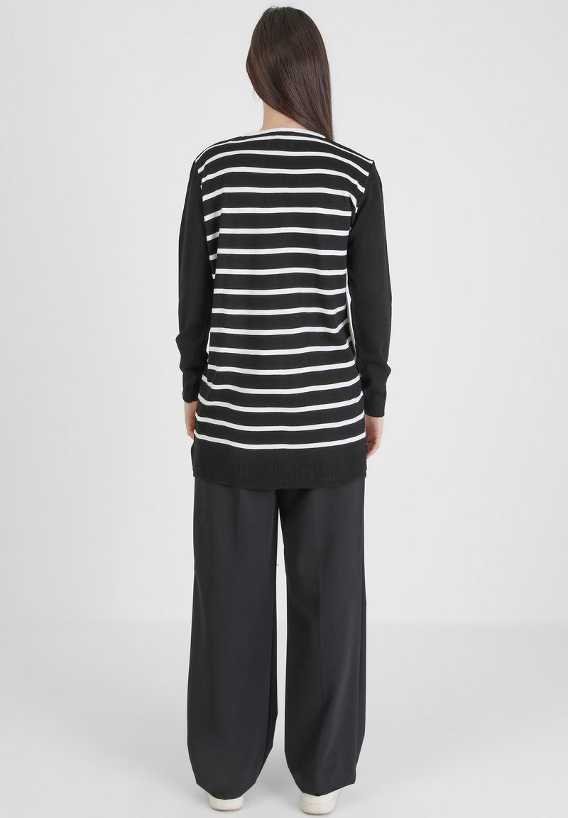 Maglietta a maniche lunghe a righe bianche e nere abbinata a pantaloni neri a gamba larga. Il tessuto sembra morbido con una vestibilità comoda e scollatura a costine.