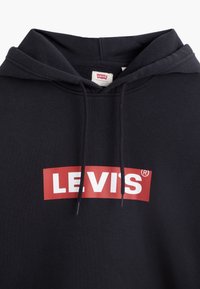 Čierna mikina s kapucňou vyrobená z jemného materiálu, ktorá má červený obdĺžnikový logo s nápisom "LEVI'S" v bielej farbe. Obsahuje kapucňu so šnúrkami a etiketu vo vnútri.