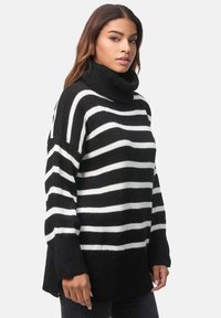 Schwarz-weißer gestreifter Strickpullover mit hohem Rollkragen, überschnittenen Schultern und Seitenschlitzen. Weiche Textur und entspannte Passform.