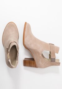 Bottes cheville en daim beige avec un talon bloc, côtés découpés et une bride réglable. Talon texturé et surface supérieure lisse.