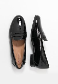 Mocassins en cuir verni noir avec un bout arrondi, un détail subtil de bride avant et un talon bas. Surface lisse avec une finition brillante.