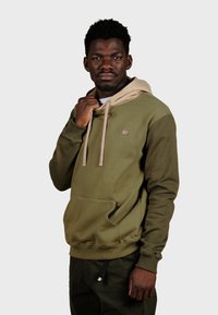 Haut à capuche vert olive avec une capuche beige, une poche kangourou et un petit logo d'éléphant. Fabriqué avec un tissu doux et des poignets côtelés.