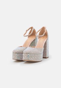 Talons compensés scintillants avec un gros talon transparent. Recouverts de minuscules strass irisés, présentant une bride à la cheville et une semelle nude.