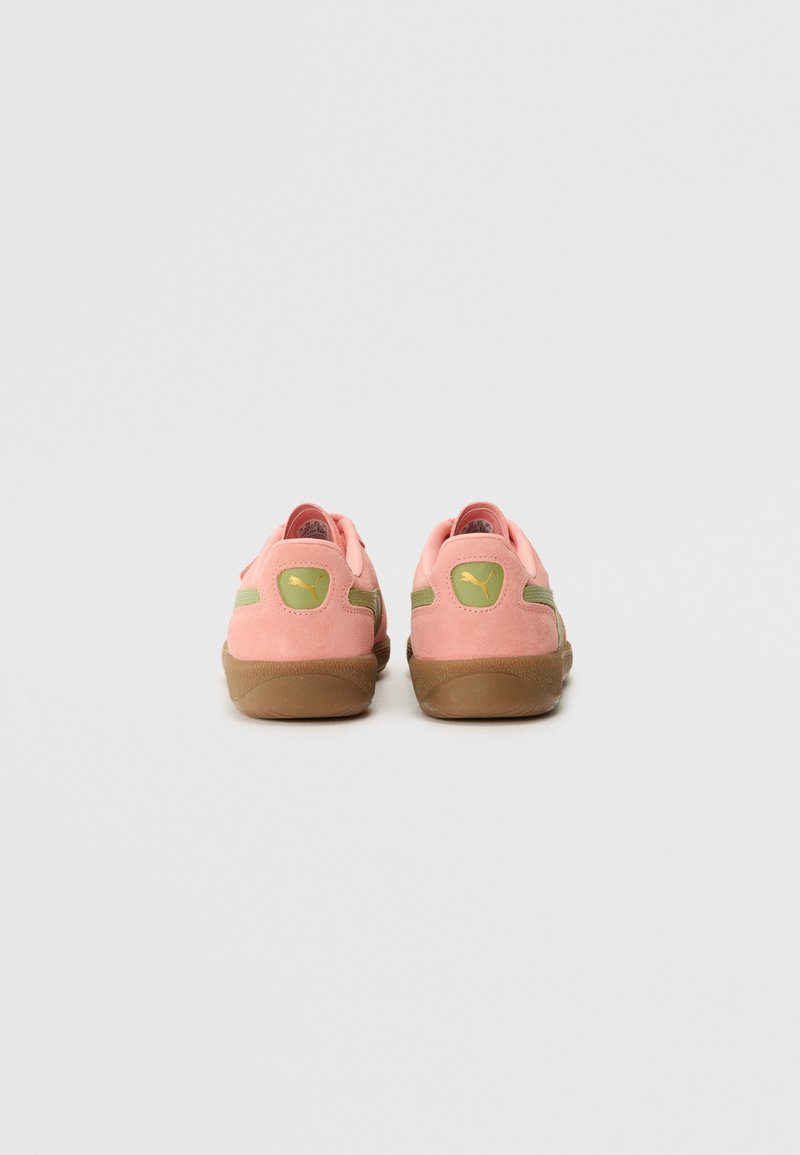 Baskets Puma avec une tige en daim rose, des accents verts et une semelle en caoutchouc brun. La vue arrière montre les détails du logo et la construction de la chaussure.