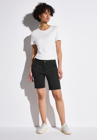 Pantalones cortos negros con bolsillos frontales y cierre de botón, combinados con una camiseta blanca lisa y zapatillas blancas. Diseño simple y ajustado.