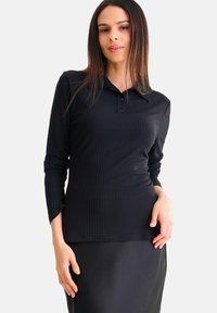Zwarte geribbelde polo met lange mouwen, voorzien van een kraag, een drie-knopen sluiting en een aansluitend ontwerp. Gecombineerd met een elegante zwarte rok.