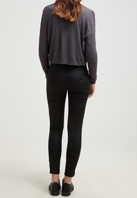 Beskuren grå långärmad topp med avslappnad passform, kombinerad med svarta slim-fit byxor och svarta sneakers; synlig tygtextur och sömdetaljer.