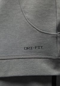 Felpa DRI-FIT grigia in tessuto, caratterizzata da una texture liscia, una leggera brillantezza e dettagli di cucitura. Logo in evidenza in nero.