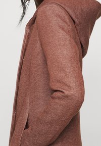 Felpa con cappuccio in tessuto marrone, textured, con chiusura frontale, tasche laterali e cappuccio. Vestibilità slim con un sottile motivo intrecciato.