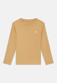 Beige langermet t-skjorte med rund hals og liten hvit "cK" logo på venstre bryst, flatlagt på en hvit bakgrunn.