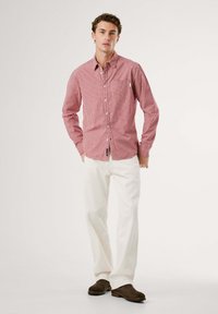 Ein rot-weiß kariertes Button-up-Hemd mit Kentkragen, langen Ärmeln und einem kleinen Logotag, kombiniert mit weißen Hosen.