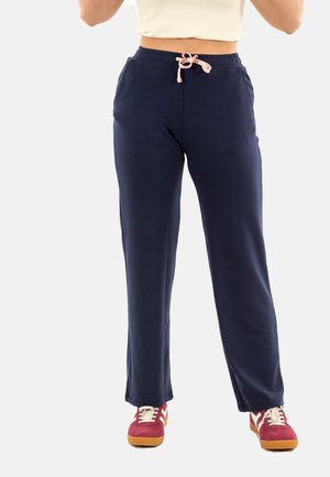 Pantalones jogger azul marino, tejido suave, cinturilla elástica con cordón rosa, bolsillos laterales, combinados con zapatillas rojas y crema.