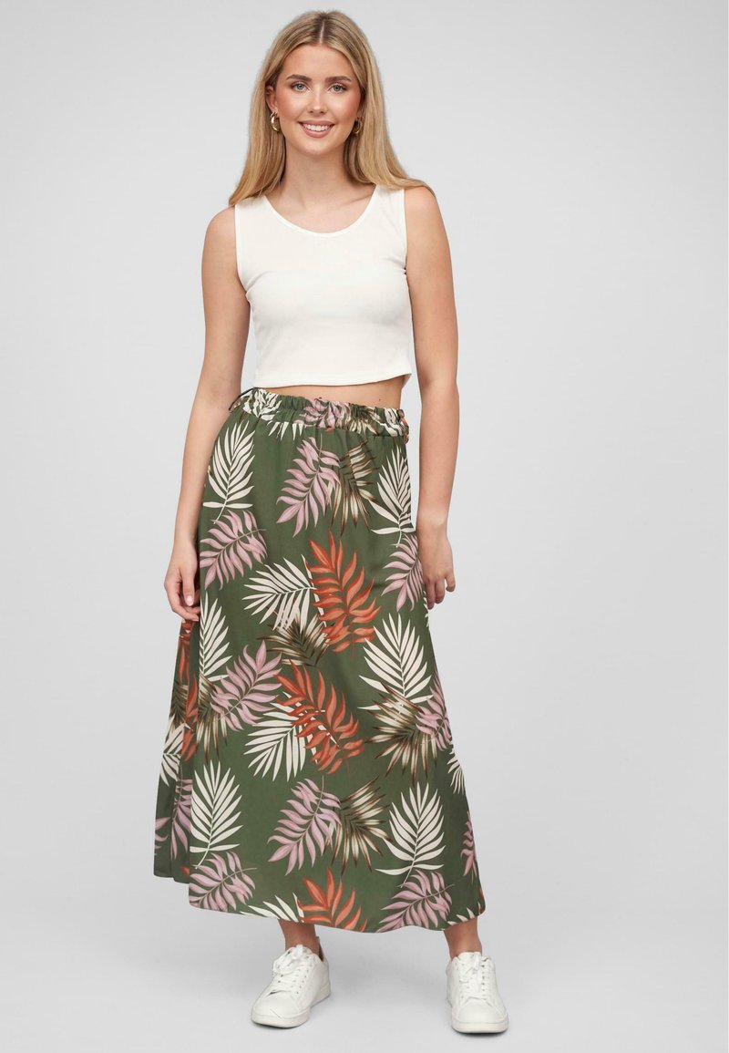 Gonna maxi in tessuto verde con motivi di foglie rossi e arancioni; vita elasticizzata; abbinata a una maglietta cropped bianca e sneakers bianche.