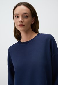 Felpa blu navy con colletto rotondo, spalle scese e una trama liscia. Design semplice senza motivi o accenti visibili.