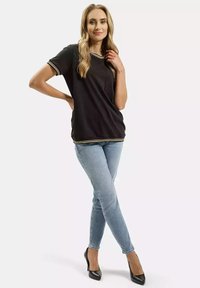 Czarny t-shirt z kieszonką na piersi, białe i złote wykończenia przy dekolcie i rękawach, zestawiony z jasnoniebieskimi obcisłymi dżinsami i czarnymi szpilkami.