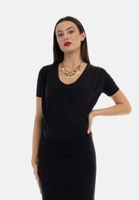 Abito nero in maglia a maniche corte con design avvolgente, caratterizzato da una silhouette aderente e un collo a barca. Accentuato da un collier d'oro a strati.