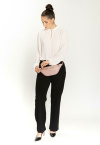 Rosa Faux-Leder Taillentasche mit einer strukturierten Oberfläche und goldenen Details, kombiniert mit einem weißen Langarmoberteil und schwarzen Hosen.