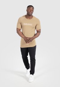 Tight passform T-shirt med "SMILODOX" text, tillsammans med svarta byxor och vita sneakers. Slät tyg, korta ärmar och rundhals.