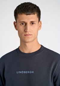 Marinblå sweatshirt med rund halsringning och ljusblått "LINDBERGH"-tryck på bröstet, tillverkad av ett mjukt tyg med en avslappnad passform.