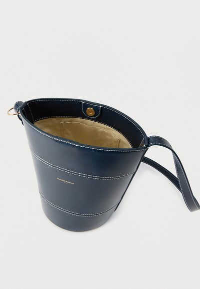Τσάντα κουβάς από δέρμα σε ναυτικό μπλε με λευκή ραφή, εσωτερική τσέπη μπεζ, μαγνητικό κλείσιμο και ρυθμιζόμενο λουρί.