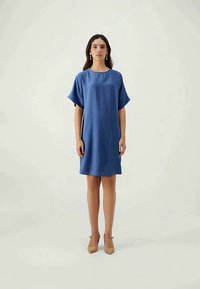 Blue short-sleeve dress with a relaxed fit. Smooth texture, knee-length. Worn with beige high-heeled shoes, simple accessories included.