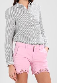 Camicia a righe bianco e nera, abbinata a pantaloni corti di denim rosa con bordo in pizzo floreale all'orlo.