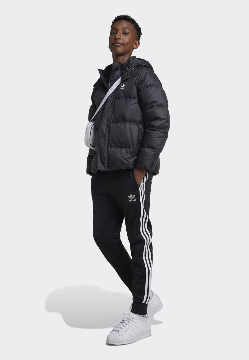 Black padded jacket with hood, white logo, black pants with white side stripes, and white sneakers. Simple design with a relaxed fit.