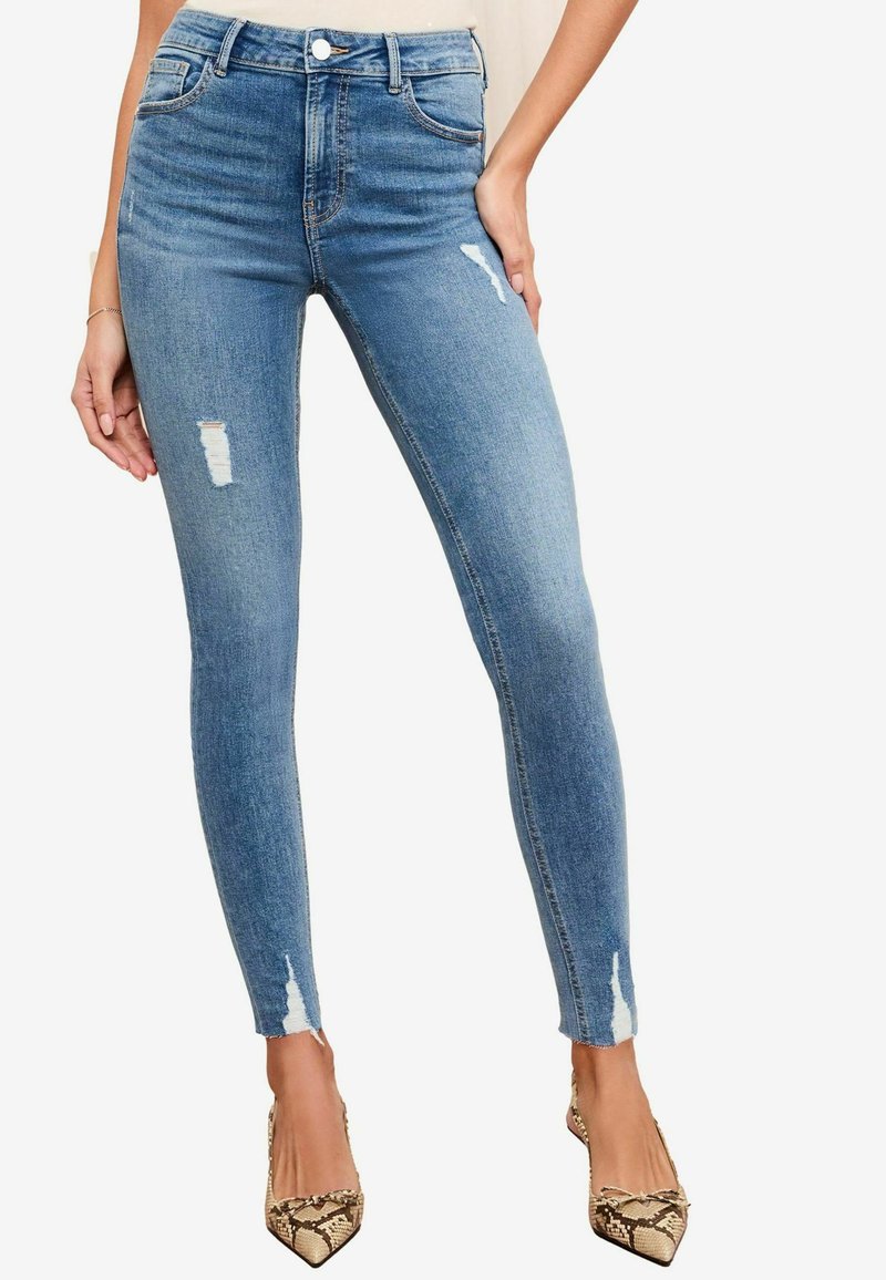 Rohked sinised teksapüksid, millel on kulumise detailid põlvedes, kõrge vöökoht ja õmblusteta disain, koos terava nina mudi nahka jäljendavate kontsadega.