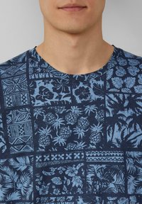 Marineblauw T-shirt met een patchwork van lichtblauwe tropische patronen, waaronder ananassen en bloemmotieven, en met een ronde hals.
