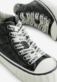 Czarne dżinsowe sneakersy za kostkę z białymi sznurówkami, z powtarzającym się tekstem, gumowym noskiem i teksturowaną podeszwą. Akcentowane białymi paskami.