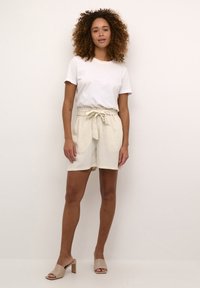 Linned shorts i lys beige med bindebånd i taljen, parret med en hvid t-shirt med rund hals. Glat tekstur, afslappet pasform, længde til midten af låret.