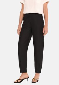 Czarne, wysokie spodnie o prostym kroju, z gładką teksturą i bocznymi kieszeniami, w zestawieniu z czarnymi sandałami na obcasie.