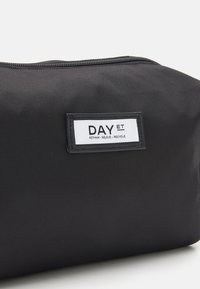 Zwarte nylon pouch met een gestructureerd oppervlak, voorzien van een wit label met "DAY ET" en een recycling slogan. Ritsluiting aan de bovenkant.