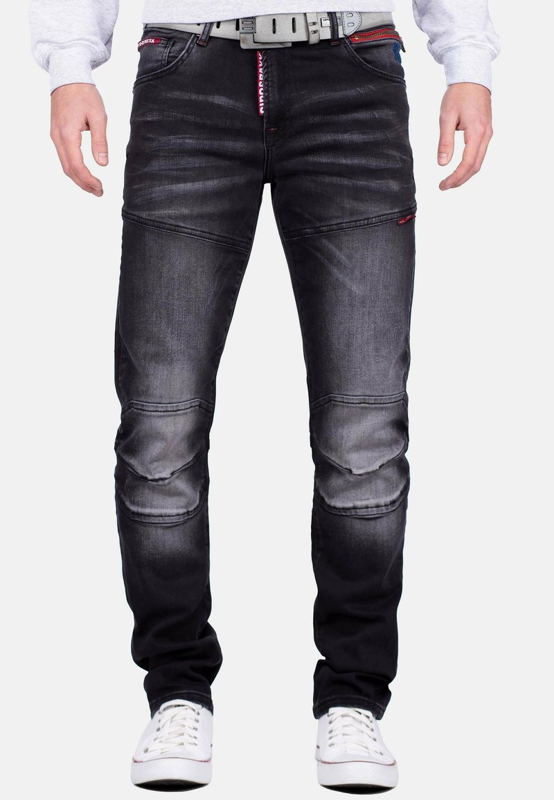 Jeans in denim nero con una finitura sbiadita, caratterizzati da pannelli sulle ginocchia, dettagli rossi e una cintura testurizzata. Progettati con una vestibilità slim e cuciture a contrasto.