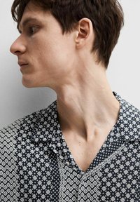 Camicia a righe bianche e nere con motivi geometrici, colletto corto e una texture di tessuto morbida; modello di profilo, con focus sul scollo.