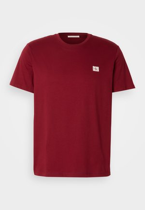 Bordeaux katoenen t-shirt met een ronde hals, korte mouwen en een klein logo-patch op de linkerborst. Glad textuur, casual ontwerp.
